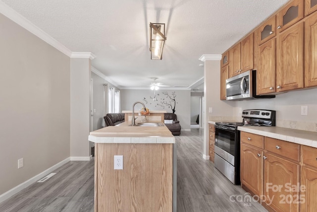 kitchen featuring a center island with sink, appliances with stainless steel finishes, ornamental molding, wood finished floors, and a sink