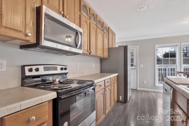 kitchen with a textured ceiling, stainless steel appliances, baseboards, dark wood finished floors, and glass insert cabinets