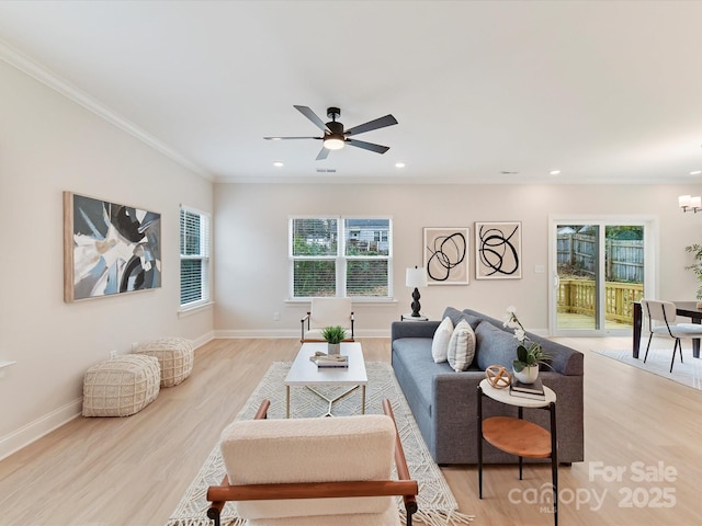 living area featuring light wood-type flooring, ornamental molding, ceiling fan with notable chandelier, and a healthy amount of sunlight