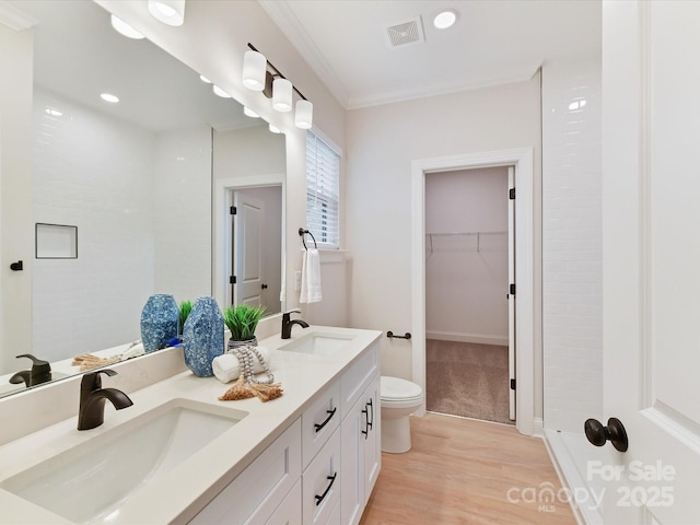 bathroom featuring visible vents, a sink, a walk in closet, and wood finished floors