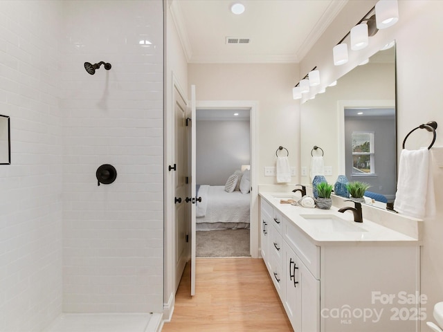 ensuite bathroom with visible vents, wood finished floors, a sink, connected bathroom, and tiled shower