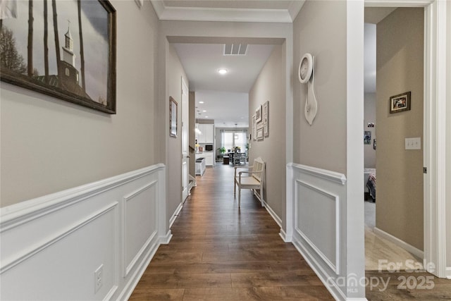 hallway featuring a wainscoted wall, visible vents, dark wood finished floors, and a decorative wall