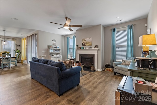 living room with a fireplace with flush hearth, visible vents, wood finished floors, and a ceiling fan