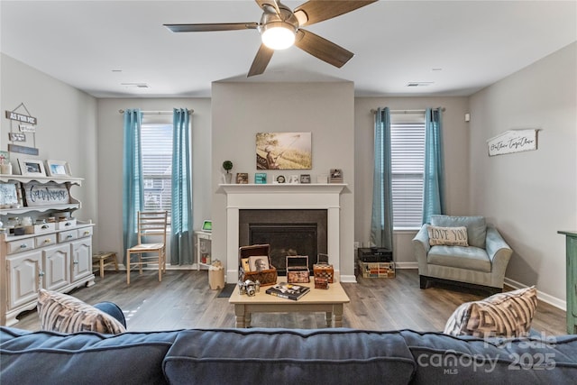 living room featuring baseboards, visible vents, a ceiling fan, wood finished floors, and a fireplace