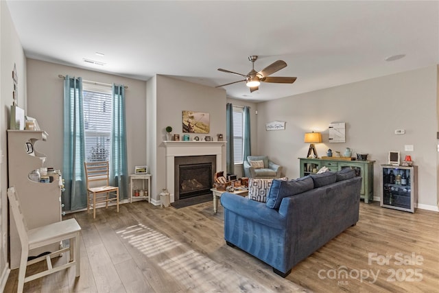 living room featuring baseboards, a ceiling fan, a fireplace with flush hearth, wine cooler, and wood finished floors