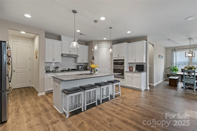 kitchen with stone counters, a center island with sink, tasteful backsplash, white cabinets, and a kitchen bar