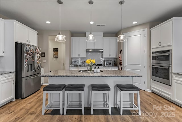 kitchen with stainless steel appliances, a sink, under cabinet range hood, and a kitchen breakfast bar