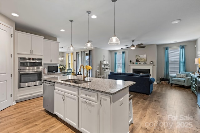 kitchen featuring stainless steel appliances, a sink, light wood-style flooring, and a center island with sink