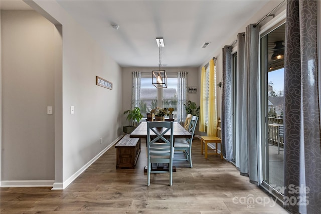 dining room with arched walkways, wood finished floors, visible vents, and baseboards