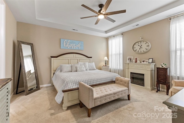 bedroom with a glass covered fireplace, multiple windows, a raised ceiling, and visible vents