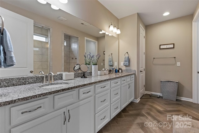 bathroom featuring double vanity, tiled shower, a sink, and baseboards