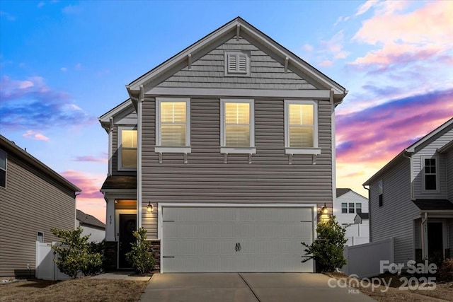 view of front facade featuring concrete driveway, an attached garage, and fence