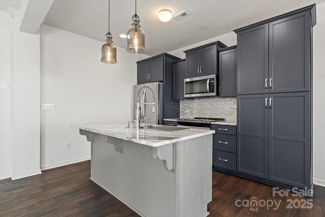 kitchen with a breakfast bar area, stainless steel appliances, dark wood-style flooring, visible vents, and a center island with sink