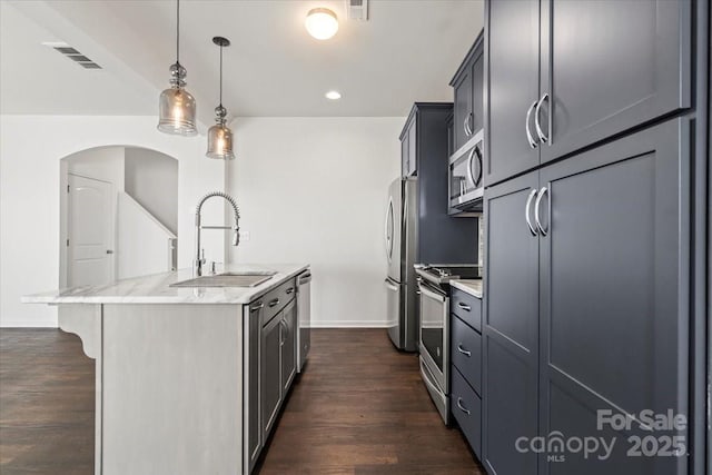 kitchen featuring light stone counters, a kitchen island with sink, stainless steel appliances, dark wood-style flooring, and a sink