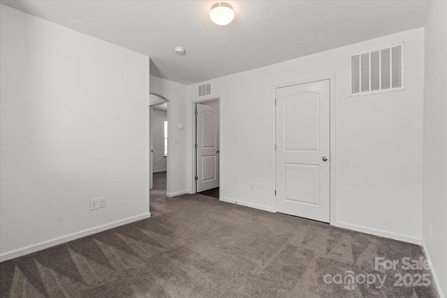 unfurnished bedroom featuring carpet, visible vents, arched walkways, and baseboards