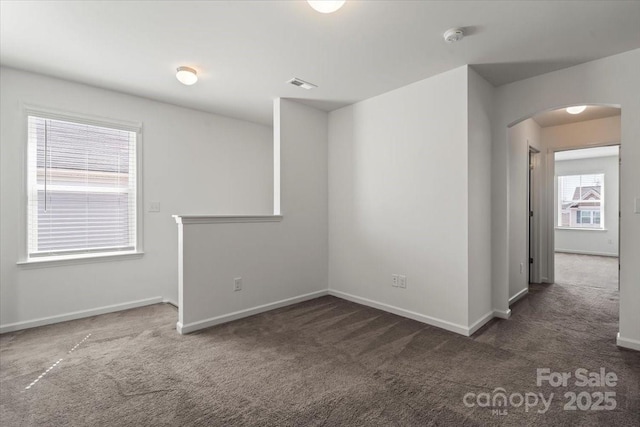 empty room with carpet floors, arched walkways, and baseboards