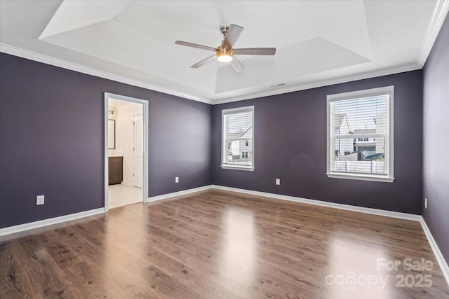 empty room with crown molding, wood finished floors, a raised ceiling, and baseboards