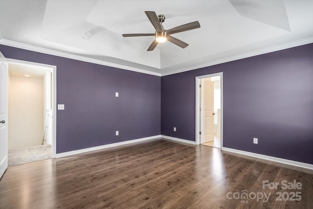 spare room with a tray ceiling, wood finished floors, and baseboards