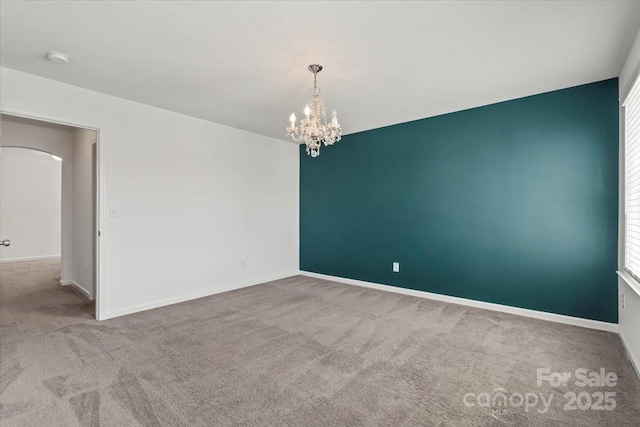 carpeted spare room featuring a chandelier, arched walkways, an accent wall, and baseboards