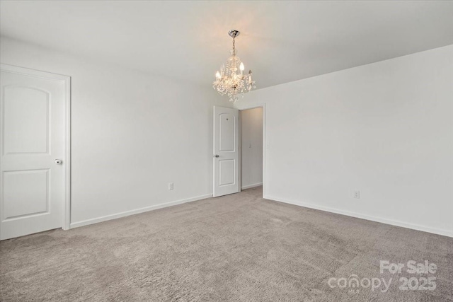 carpeted spare room featuring baseboards and an inviting chandelier