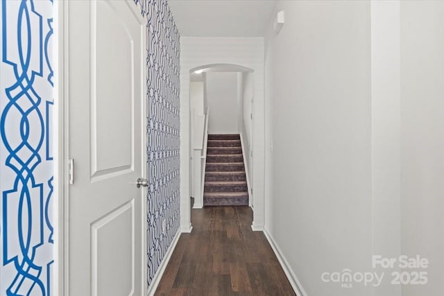 corridor featuring baseboards, stairs, wood finished floors, and arched walkways