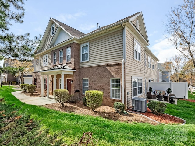 back of property with central AC unit, a lawn, fence, and brick siding