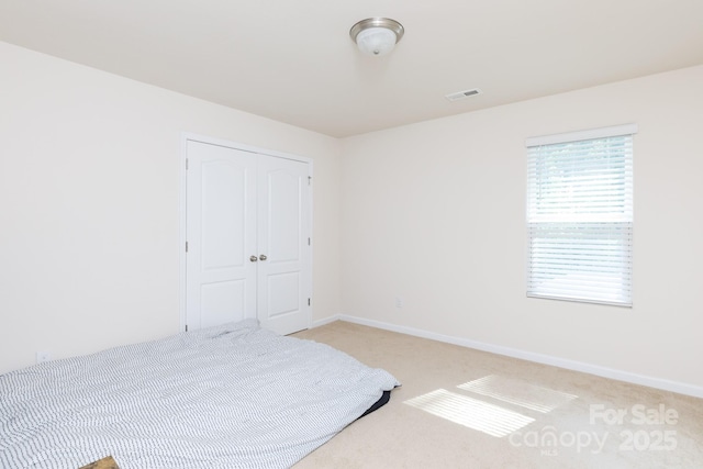 unfurnished bedroom with light carpet, a closet, visible vents, and baseboards