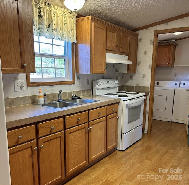 kitchen featuring white electric stove, brown cabinets, washer and dryer, under cabinet range hood, and a sink