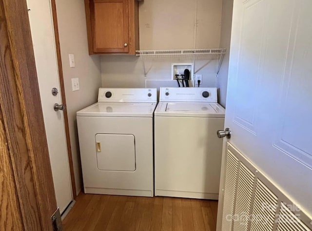 clothes washing area with cabinet space, washing machine and dryer, and hardwood / wood-style floors