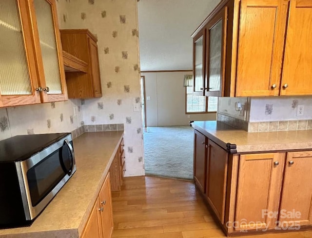 kitchen with light wood finished floors, stainless steel microwave, brown cabinets, and wallpapered walls