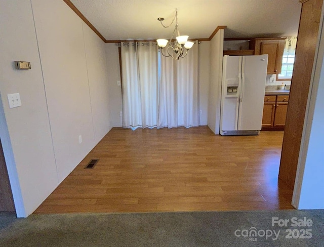 kitchen with ornamental molding, white refrigerator with ice dispenser, brown cabinets, and visible vents