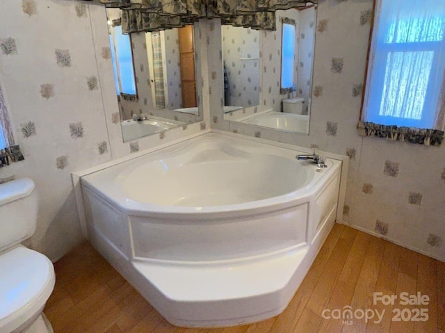 full bath featuring a bath, wood finished floors, toilet, and wallpapered walls