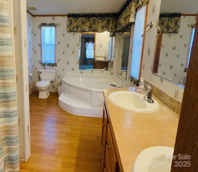 bathroom with toilet, wood finished floors, vanity, a bath, and wallpapered walls