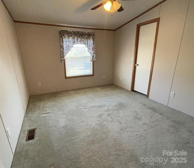 unfurnished bedroom with a ceiling fan, carpet flooring, visible vents, and crown molding