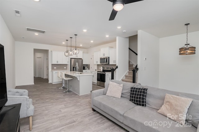 living room featuring stairway, visible vents, light wood-style floors, and recessed lighting