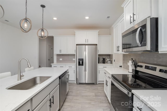 kitchen with light wood-style flooring, appliances with stainless steel finishes, decorative light fixtures, light countertops, and a sink