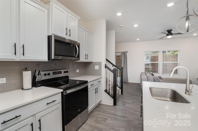 kitchen featuring stainless steel appliances, light countertops, backsplash, open floor plan, and a sink