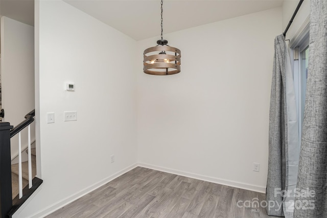 unfurnished dining area with a notable chandelier, baseboards, and wood finished floors