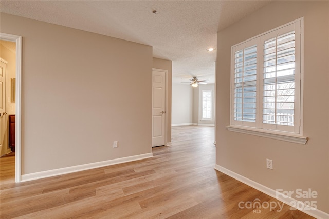 spare room with light wood-style floors, ceiling fan, a textured ceiling, and baseboards