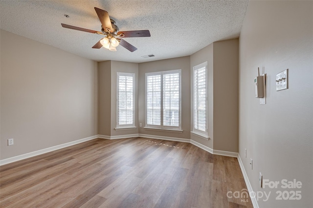 spare room featuring a textured ceiling, wood finished floors, a ceiling fan, visible vents, and baseboards