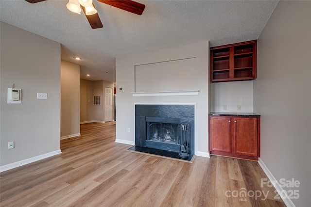 unfurnished living room featuring a textured ceiling, baseboards, a fireplace with flush hearth, and light wood-style floors