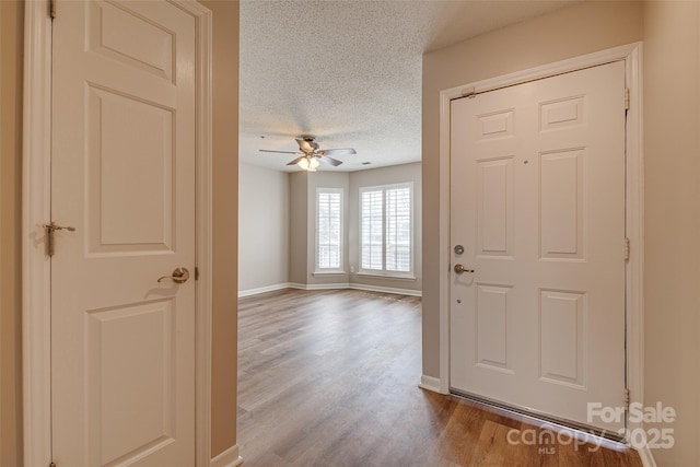 entryway with dark wood-type flooring, a textured ceiling, baseboards, and a ceiling fan