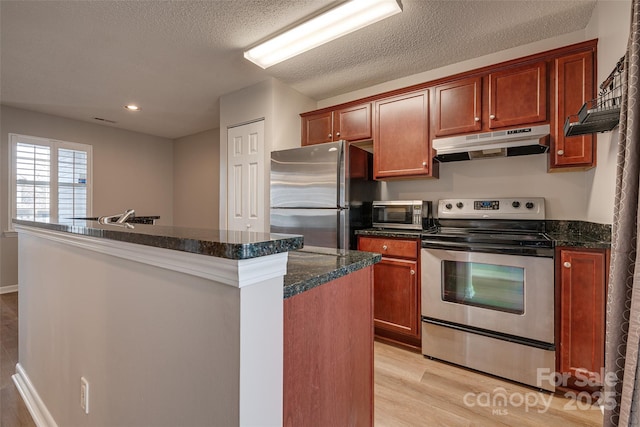 kitchen featuring a textured ceiling, under cabinet range hood, stainless steel appliances, a kitchen island, and light wood finished floors