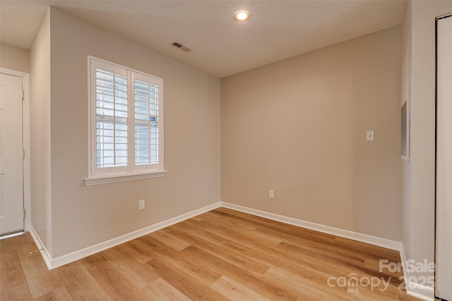 spare room with light wood-style floors, visible vents, and baseboards