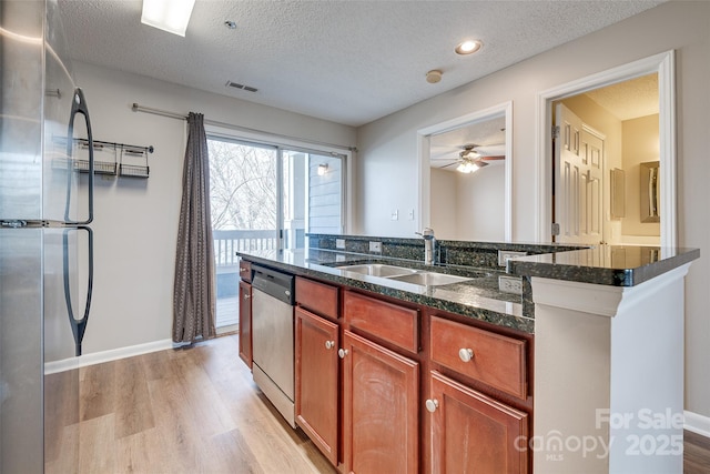 kitchen featuring a textured ceiling, stainless steel appliances, a sink, light wood-style floors, and dark stone countertops