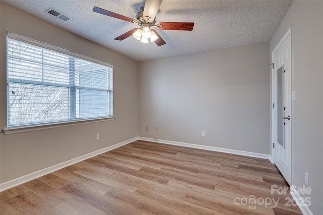 empty room featuring visible vents, a textured ceiling, and light wood finished floors