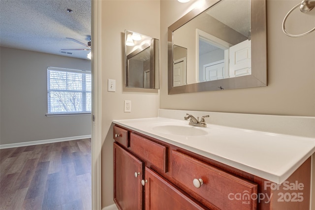 bathroom featuring a ceiling fan, a textured ceiling, vanity, wood finished floors, and baseboards