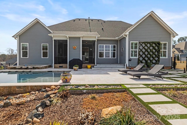 back of house featuring fence, roof with shingles, a sunroom, a fenced in pool, and a patio area