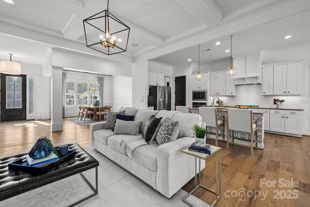 living area featuring an inviting chandelier, coffered ceiling, light wood finished floors, and beam ceiling