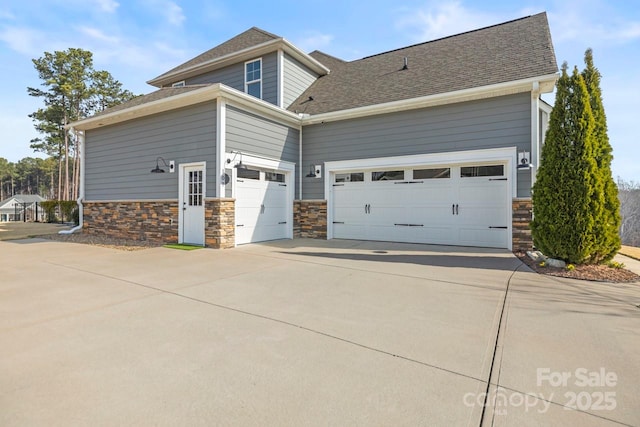 view of home's exterior with concrete driveway, a garage, stone siding, and a shingled roof